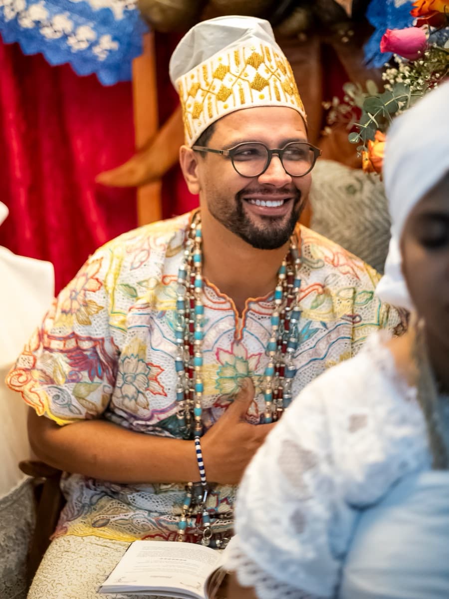 Babá Diego de Odé, de branco, contas e filá bordado, sorri durante o lançamento de seu primeiro livro.